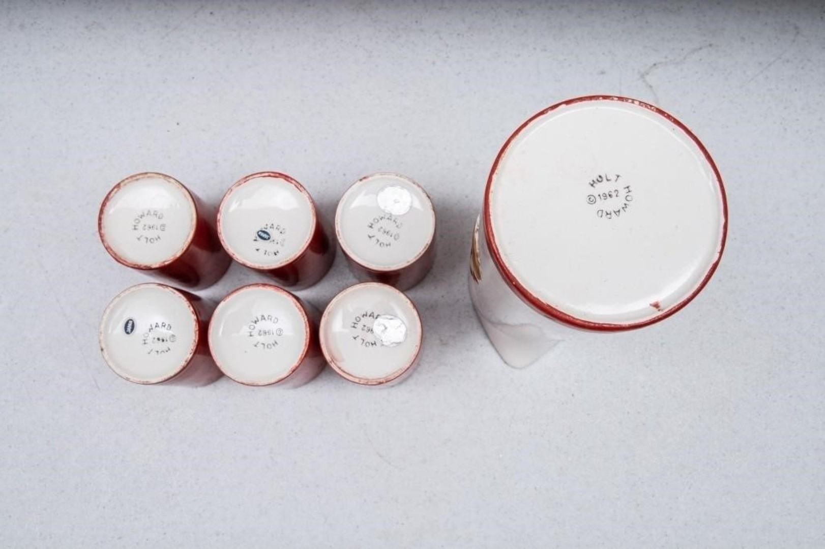 Undersides of Holt Howard Coq Rouge handleless juice pitcher and six cups showing 1962 backstamps.