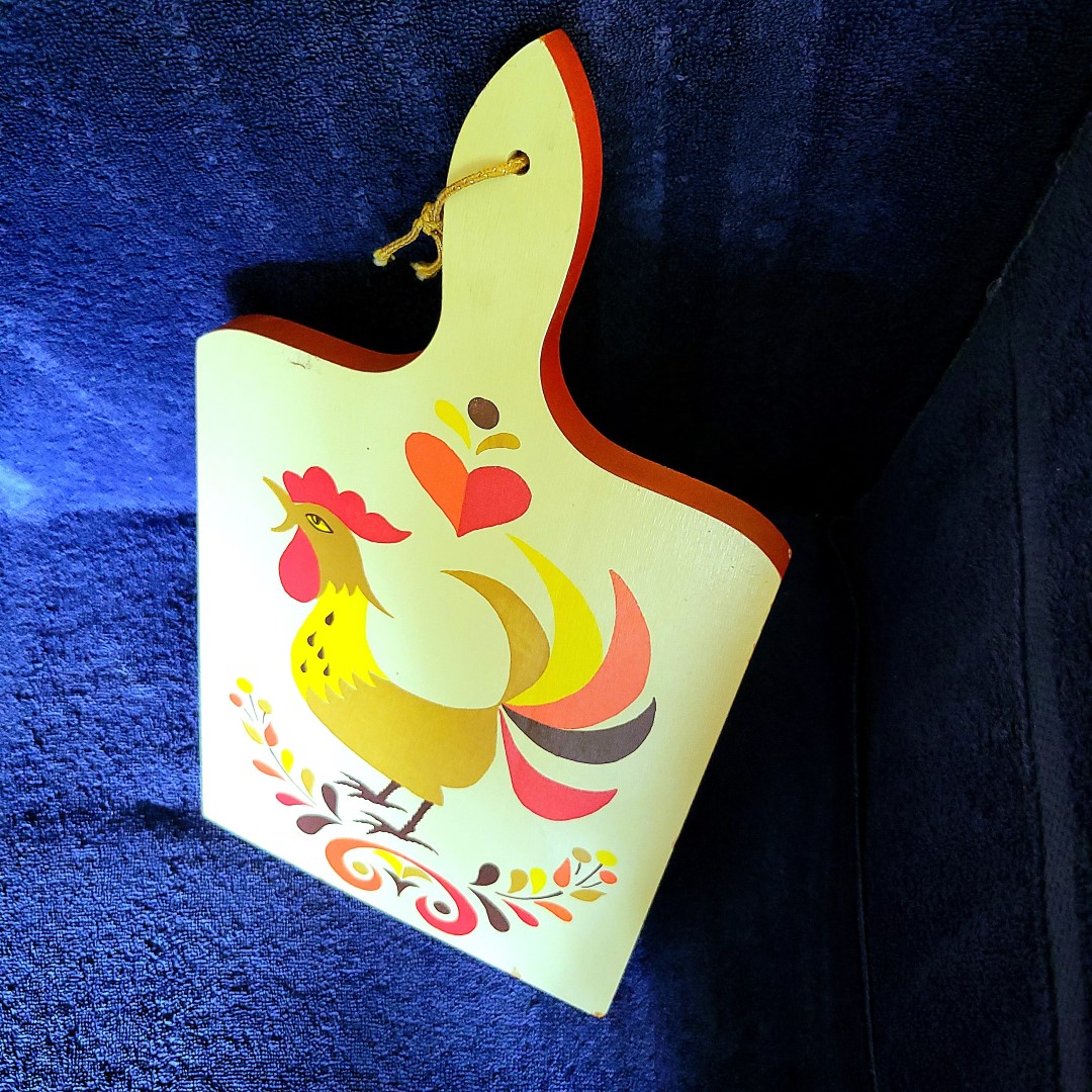 Angled view of Holt Howard Coq Rouge cutting board showing painted edge and hanging cord.
